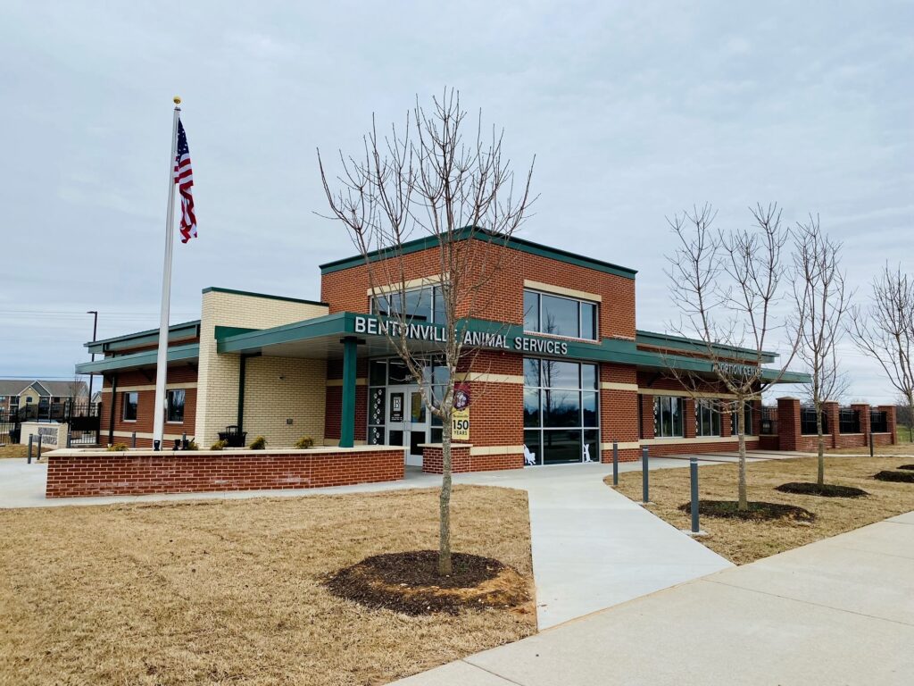  A brick building with the sign "Bentonville Animal Services" displayed prominently. An American flag is beside the building.
